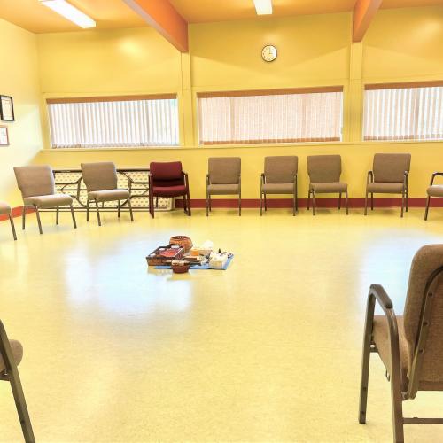 group room with many grey chairs sitting in a circle with a couple dark red chairs for elders