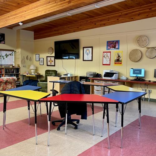 learning centre with drums on the wall, a tv, and tables that form a circle surrounding a teachers chair